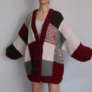 Może przedstawiać: Kardigan w stylu patchwork w odcieniach bordowego, kremowego, zielonego i szarego. Sweter o dużym rozmiarze ma zapinany na guziki przód i gruby wzór dzianiny. Rękawy są długie i obszerne, co dodaje przytulnej estetyki.