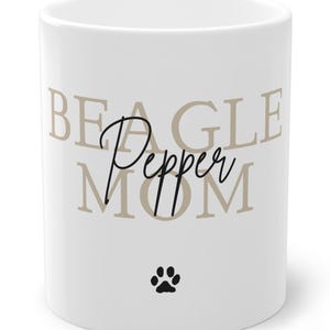 Könnte beinhalten: Weiße Keramik-Tasse mit dem Schriftzug "BEAGLE MOM" in beiger Schrift, dem Namen "Pepper" in Schreibschrift und einem schwarzen Pfotenabdruck. Ein tolles Geschenk für Beagle-Besitzer.