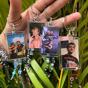 Puede incluir: Cuatro llaveros de plástico transparente con abalorios de cuentas de colores. Cada llavero presenta una fotografía diferente de una persona o un grupo de personas. Las fotos son en color y parecen ser de la década de 1990.