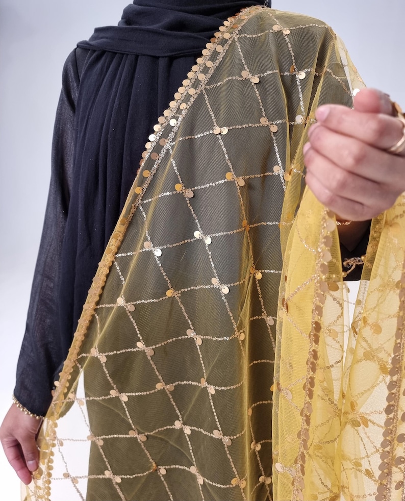 May include: A yellow sheer scarf with gold sequins arranged in a grid pattern. The scarf has a gold fringe border.