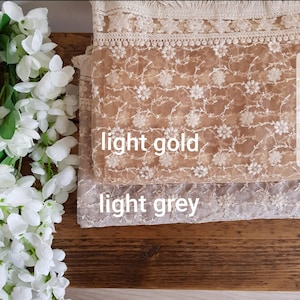 May include: Two layers of sheer fabric with floral embroidery. The top layer is light gold and the bottom layer is light grey.