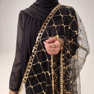 May include: A black sheer shawl with gold coin embellishments. The shawl has a delicate net-like texture and is adorned with a border of gold coins.