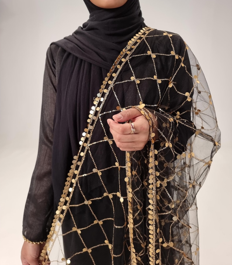 May include: A black sheer shawl with gold coin embellishments. The shawl has a delicate net-like texture and is adorned with a border of gold coins.