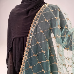 May include: A teal net scarf with gold sequins and a gold beaded border. The scarf is draped over a black shirt.
