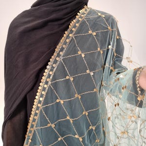 May include: A light blue sheer scarf with gold sequins arranged in a grid pattern. The scarf has a gold trim with sequins around the edges.