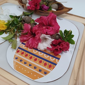 Puede incluir: Un bodegón con flores coloridas, incluyendo flores rojas, blancas y amarillas, dispuestas sobre manteles individuales ovalados decorativos. Los manteles individuales tienen un patrón amarillo y azul. Un cuenco de madera con piedras decorativas está en el fondo.