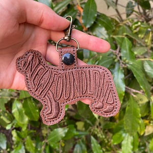 May include: A brown leather keychain in the shape of a Bloodhound dog. The word "BLOODHOUND" is stitched into the design. The keychain has a bronze-colored clasp and a black button.