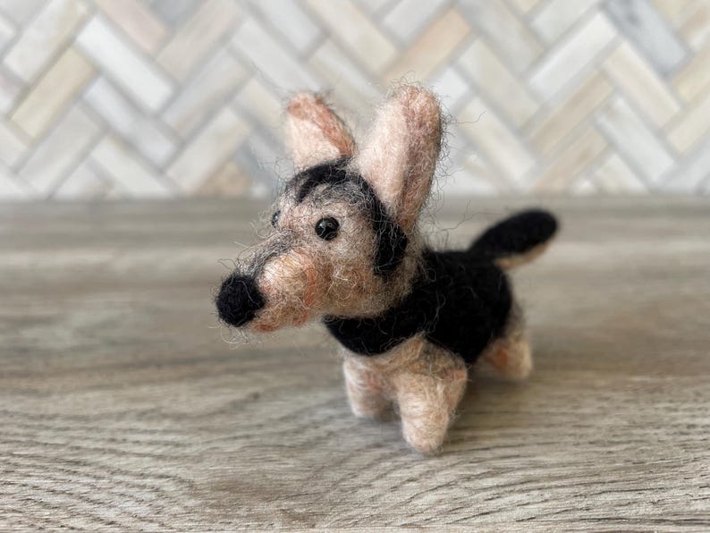 May include: A small, hand-felted dog figurine with black and brown fur. The dog has a long snout and floppy ears.