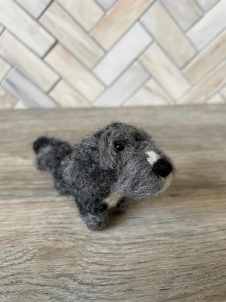 May include: A gray and white needle felted dog figurine. The dog is sitting up with its head tilted up and its tongue sticking out.