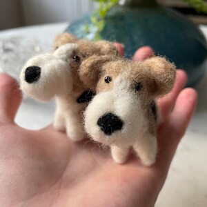 May include: Two small, hand-felted dog figurines. The dogs are brown and white with black noses and eyes. They are sitting on a person's hand.
