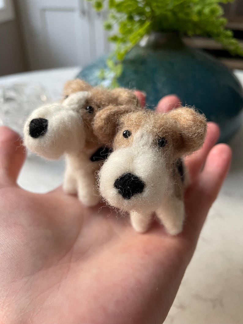 May include: Two small, hand-felted dog figurines. The dogs are brown and white with black noses and eyes. They are sitting on a person's hand.