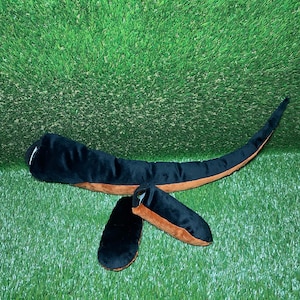 Peut inclure: Une queue en peluche noire et marron avec un embout en peluche noir et marron séparé. La queue est longue et incurvée, et l'embout est petit et rond.
