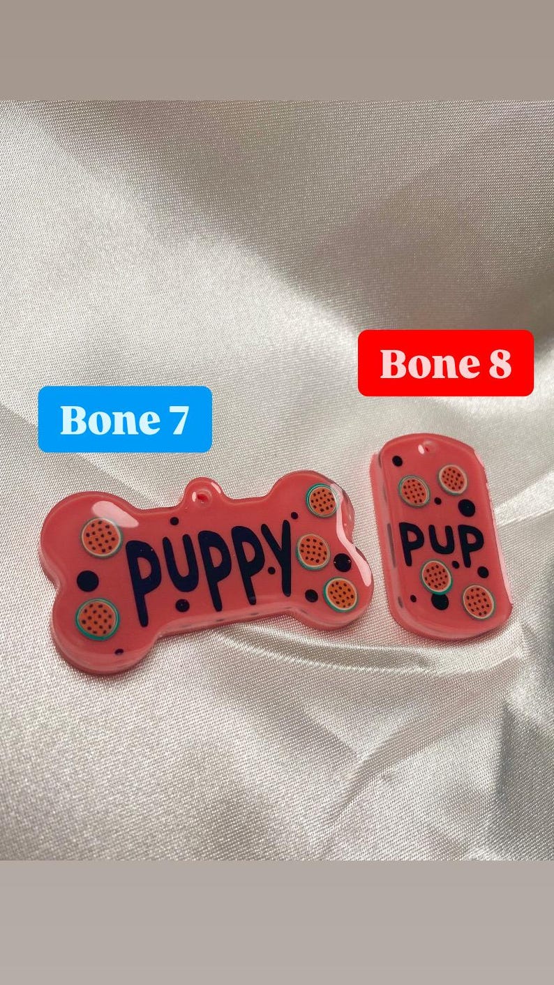 May include: Two pink pet tags with a watermelon design. One tag is bone-shaped and says "PUPPY" in dark blue letters. The other tag is rectangular and says "PUP." Both tags have a hole for attaching to a collar.