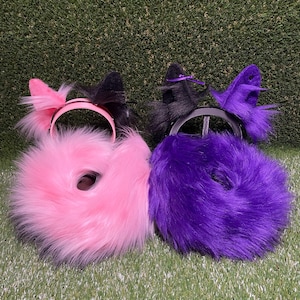 May include: Two sets of cat ears and tails. One set is pink, the other is purple. The ears are attached to headbands. The tails are fluffy and round. The ears and tails are made of faux fur.