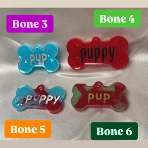 May include: Four dog bone-shaped pet tags in various colors. The tags are labeled "Pup" and "Puppy" in different fonts. The tags are blue, red, and green with glitter accents. The tags are labeled "Bone 3", "Bone 4", "Bone 5", and "Bone 6".