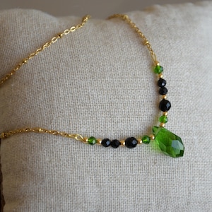 Puede incluir: Un collar de cadena dorada con cuentas de cristal negro y verde y un gran colgante de cristal verde.