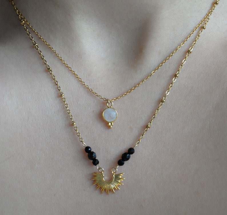 May include: A gold layered necklace with a white moonstone pendant and a sunburst charm with black beads.