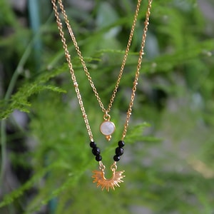 May include: A gold layered necklace with a moonstone pendant and black beads. The bottom layer features a sunburst design.