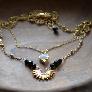 May include: A gold chain necklace with a white stone pendant and black beads. The pendant is a sunburst design.