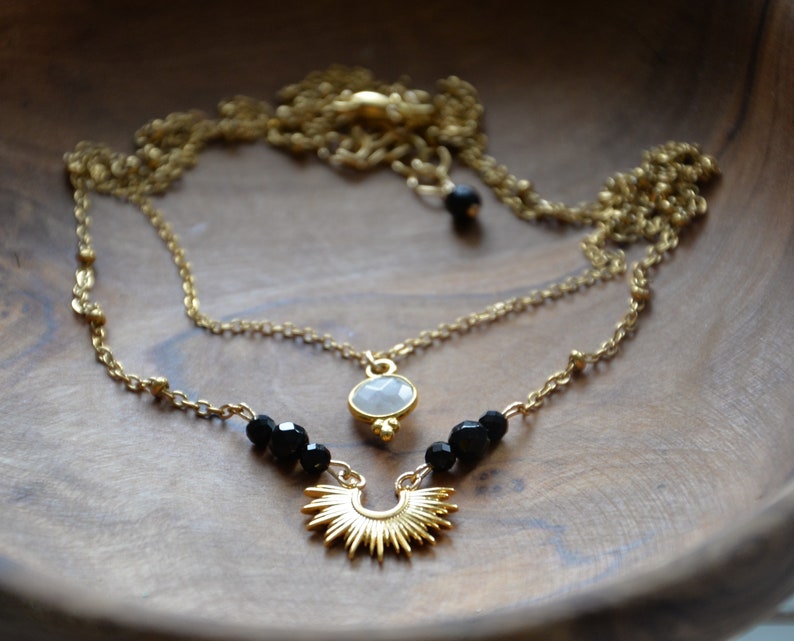 May include: A gold chain necklace with a white stone pendant and black beads. The pendant is a sunburst design.