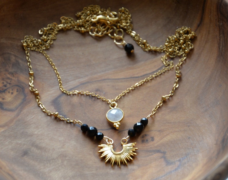 May include: A gold layered necklace with a white stone pendant, black beads, and a sunburst charm.