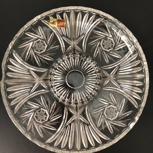 May include: A clear glass serving dish with a starburst pattern and a central dip. The dish has a raised rim and is divided into six sections.