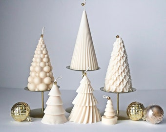 Puede incluir: Cinco velas blancas de árbol de Navidad de diferentes diseños en soportes dorados. Las velas están sobre una superficie blanca con adornos dorados.