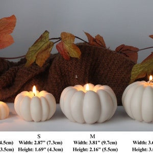 Puede incluir: Cuatro velas blancas con forma de calabaza de diferentes tama&ntilde;os, etiquetadas como XS, S, M y L. Las velas est&aacute;n encendidas y tienen una textura acanalada. Las medidas de cada tama&ntilde;o se enumeran debajo de las velas en pulgadas y cent&iacute;metros.