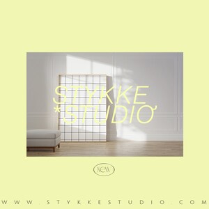 Pu&ograve; includere: Una stanza bianca con una grande finestra che lascia entrare la luce naturale. Un divano bianco si trova di fronte a un'opera d'arte a griglia in bianco e nero con il testo "STYKKE STUDIO" in giallo.