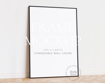 Könnte beinhalten: Ein schwarzer Rahmen-Mockup mit weißem Hintergrund. Der Rahmen steht auf einem Holzboden. Der Text "FRAME MOCKUP" ist in Weiß auf dem Rahmen geschrieben. Der Text "DIN A 4 RATIO" und "CHANGEABLE WALL COLOR" ist in Weiß unter dem Rahmen geschrieben. Der Text "YKKE STUDIO DIGITAL DESIGN MOCKUPS BY" ist in Weiß in einem Kreis unten rechts am Rahmen geschrieben.