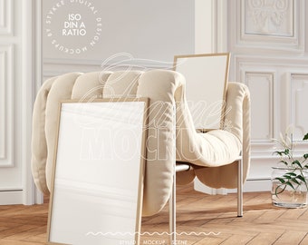 May include: A white, tufted armchair with a wooden frame and two gold picture frames leaning against it. The chair is in a room with white walls and a wooden floor.
