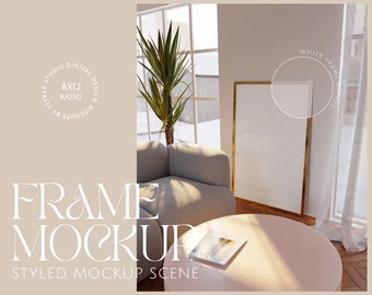 Op de afbeelding: Een gestylede mockup-scène met een wit frame met een gouden rand, een lichtgrijze fauteuil, een ronde salontafel en een boek op de tafel. Het frame is 20,32 cm x 30,48 cm en is geplaatst tegen een witte muur met een raam erachter.