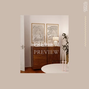May include: Two black and white line art prints of figures in a minimalist style, framed in natural wood frames, hanging on a white wall above a wooden cabinet with a white table and candles in front of it.