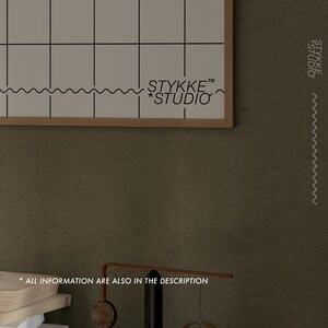 May include: A framed white grid poster with the text "STYKKE&trade; *STUDIO" at the bottom. The poster is hanging on a textured brown wall.
