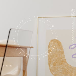 May include: A gold framed print with a white circle and the text "soft interior | natural & soft daylight | natural" around the circle. The print features a yellow and purple abstract design.