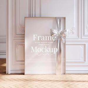 Pode incluir: Uma maquete de moldura dourada com uma fita e um laço prateados. A moldura está em um piso de madeira. O texto "Frame Mockup" está escrito na moldura.