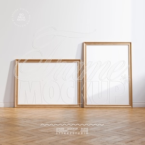 May include: Two wooden picture frames with white mounts and blank canvases, standing on a light brown wood floor with a herringbone pattern. The frames are on a white wall with a subtle shadow cast from the frames.