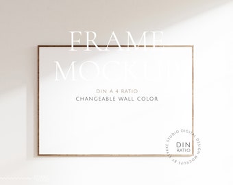 Puede incluir: Un marco rectangular de madera con interior blanco, con el texto "FRAME MOCKUP" y "DIN A 4 RATIO CHANGEABLE WALL COLOR". El marco está colocado contra una pared blanca lisa, creando una estética limpia y minimalista.