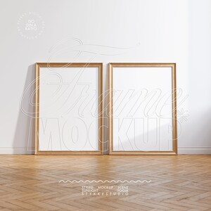 Puede incluir: Dos marcos de fotos vacíos de madera con un acabado marrón claro, de pie sobre un suelo de madera marrón claro con un patrón de espiga. Los marcos están uno al lado del otro, con el marco izquierdo ligeramente delante del marco derecho. Los marcos están contra una pared blanca.