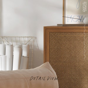 Puede incluir: Vista detallada de una habitaci&oacute;n con un puf beige claro, un mueble de madera con frente tejido y una rejilla met&aacute;lica con papel blanco enrollado. Se ve un estampado enmarcado.