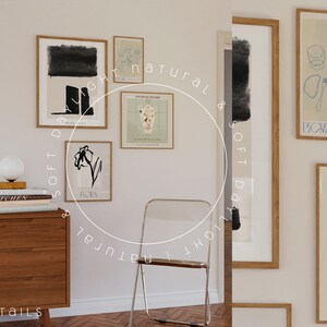 May include: A collection of framed art prints with minimalist designs, including a black and white floral print, a print with a vase of flowers, and a print with a black and white abstract design. The prints are hung on a white wall with a wooden dresser and a clear plastic chair in the foreground.