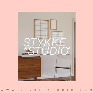 May include: A light wood dresser with three drawers, a white lamp, and a stack of books. There are four framed grid-patterned prints on the wall behind the dresser. The text "STYKKE STUDIO" is written in white on the wall. A white folding chair is in the foreground. The text "WWW.STYKKE STUDIO.COM" is written at the bottom of the image.