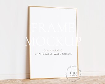 Könnte beinhalten: Ein goldener Rahmen-Mockup mit weißem Hintergrund. Der Rahmen steht auf einem Holzboden und einer weißen Wand. Der Text "FRAME MOCKUP" ist in Weiß auf dem Rahmen geschrieben. Der Text "DIN A 4 RATIO" und "CHANGEABLE WALL COLOR" ist in Weiß unter dem Rahmen geschrieben.