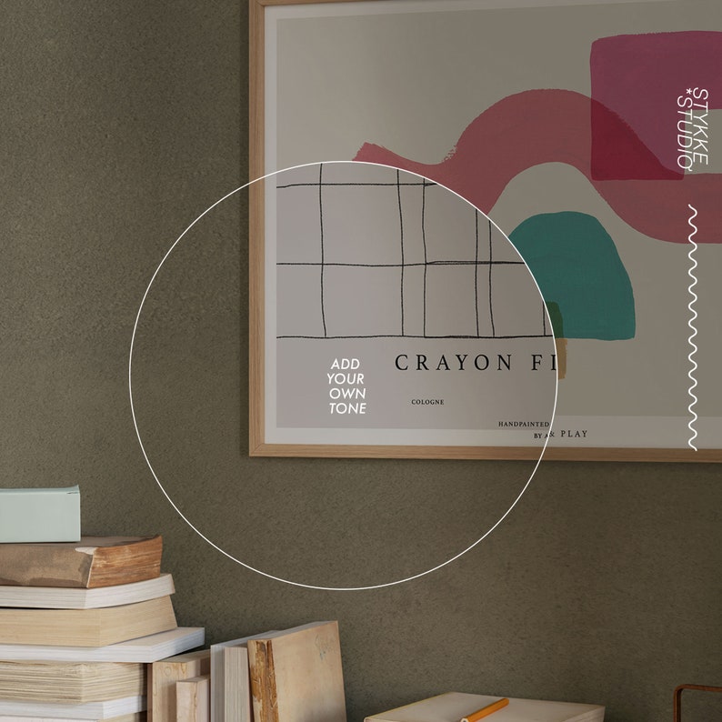 May include: A framed art print featuring a grid pattern and abstract shapes in pink, teal, and white. The text "Crayon Fix Cologne" and "Handpainted by A Play" is visible on the print. The print is hanging on a wall with a stack of books and a small box below it.