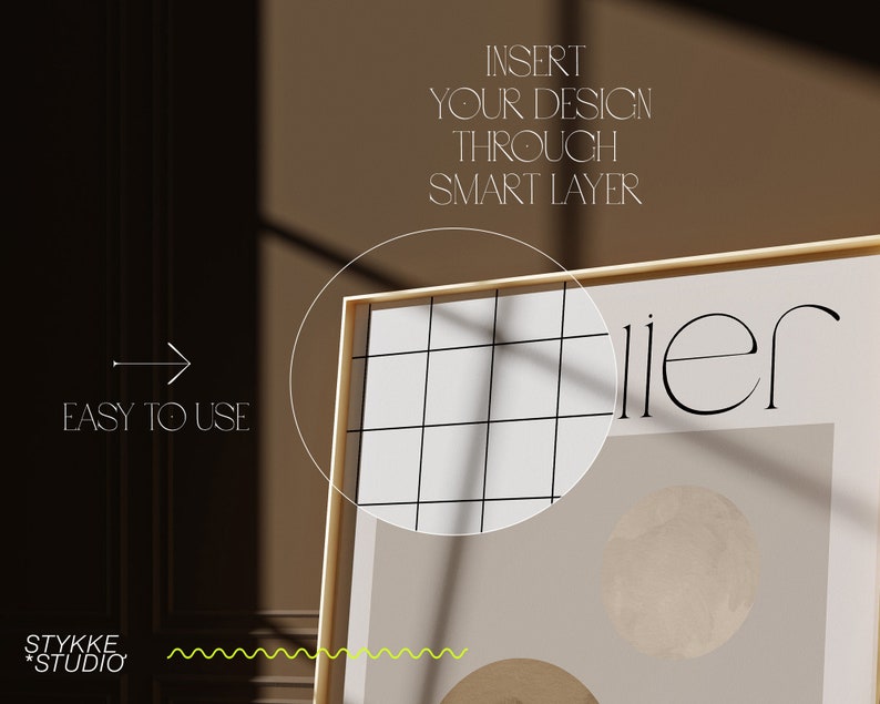 May include: A gold framed poster with a white background and a black grid pattern. The poster has the text "illier" in black and a beige circle with a textured surface.