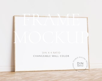Puede incluir: Una maqueta de marco blanco con un marco de madera clara, sentado en un suelo de madera. El marco está apoyado contra una pared blanca. El texto "FRAME MOCKUP" está en la parte superior del marco. El texto "DIN A 4 RATIO" y "CHANGEABLE WALL COLOR" está debajo del marco. Un círculo con el texto "STYKKE STUDIO DIGITAL DESIGN MOCKUPS" y "DIN RATIO" está en la esquina inferior derecha.