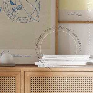 Puede incluir: Un mueble de madera clara con frente tejido exhibe una pila de revistas blancas. Arriba, impresiones art&iacute;sticas enmarcadas muestran dibujos lineales azules. El texto en la impresi&oacute;n art&iacute;stica dice "ART SERIES / ANA & YVY BLUSH". Una esfera blanca se encuentra en el mueble.