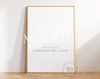 Könnte beinhalten: Ein goldener Rahmen-Mockup mit weißem Hintergrund. Der Rahmen steht auf einem Holzboden und einer weißen Wand. Der Text "FRAME MOCKUP" ist in Weiß auf dem Rahmen geschrieben. Der Text "DIN A 4 RATIO" und "CHANGEABLE WALL COLOR" ist in Schwarz unter dem Rahmen geschrieben.