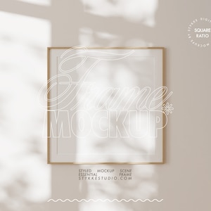 Op de afbeelding: Een gouden frame mockup met een witte achtergrond. Het frame is op een witte muur met een schaduw van een plant op de achtergrond. De tekst "Frame Mockup" is in wit op het frame geschreven.