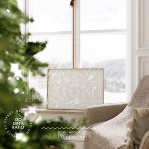 May include: A gold frame mockup with a white background and a snowy scene visible through a window. The frame is sitting on a white marble surface in front of a beige armchair.